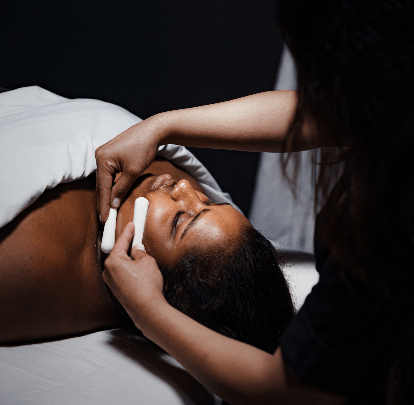 Soin du visage en spa avec une esthéticienne appliquant un traitement relaxant sur une personne allongée, dans une ambiance calme et tamisée