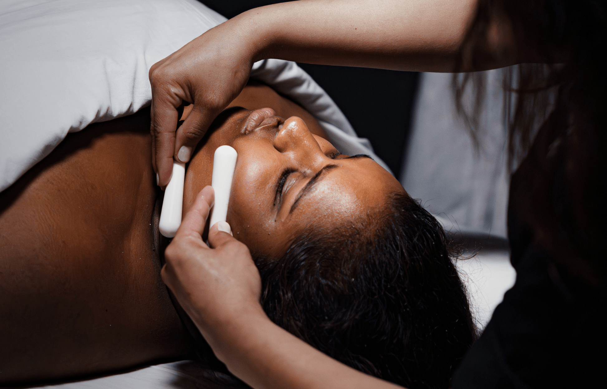 Soin du visage en spa avec une esthéticienne appliquant un traitement relaxant sur une personne allongée, dans une ambiance calme et tamisée